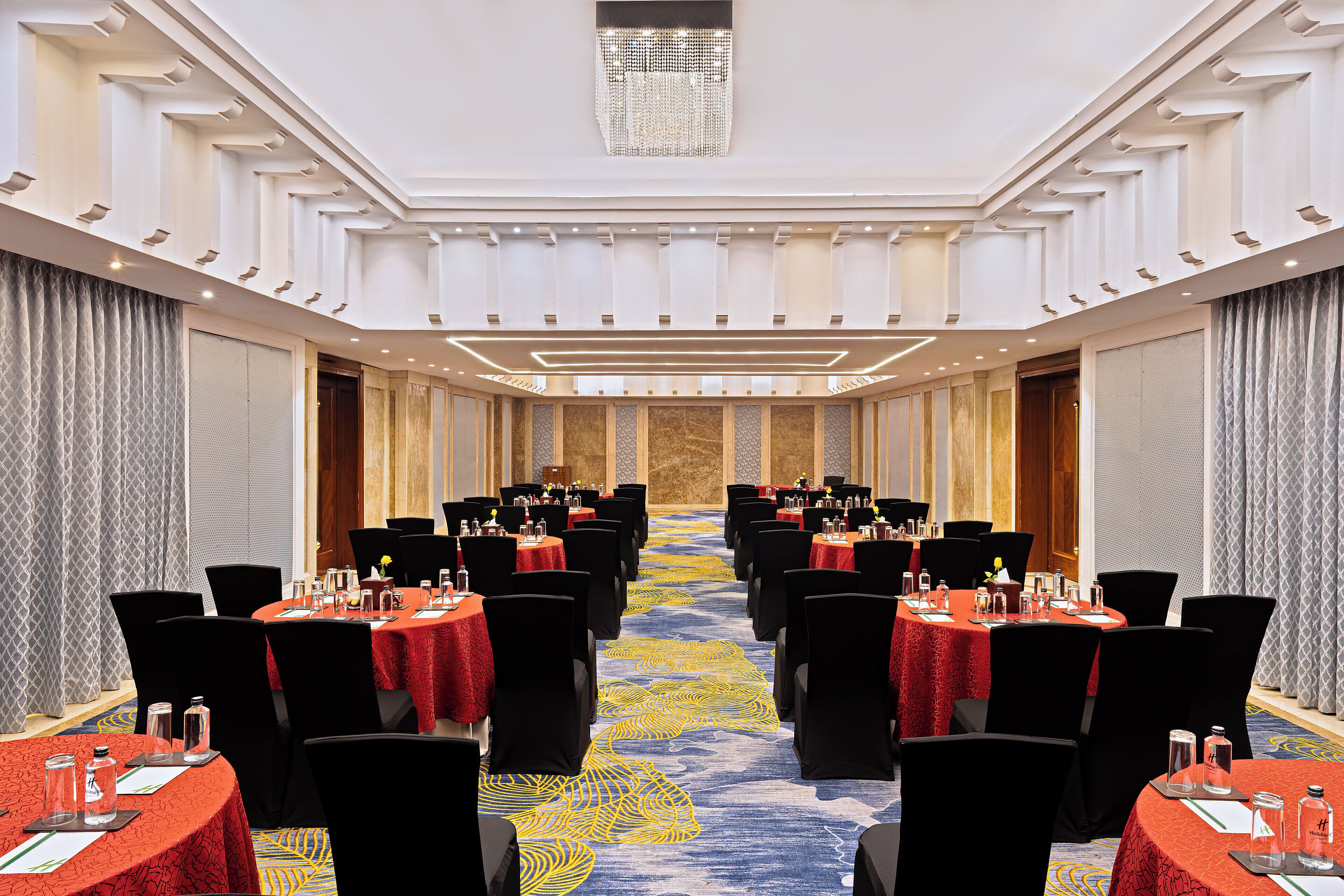 A conference room with multiple tables and chairs, a patterned carpet, and a chandelier.