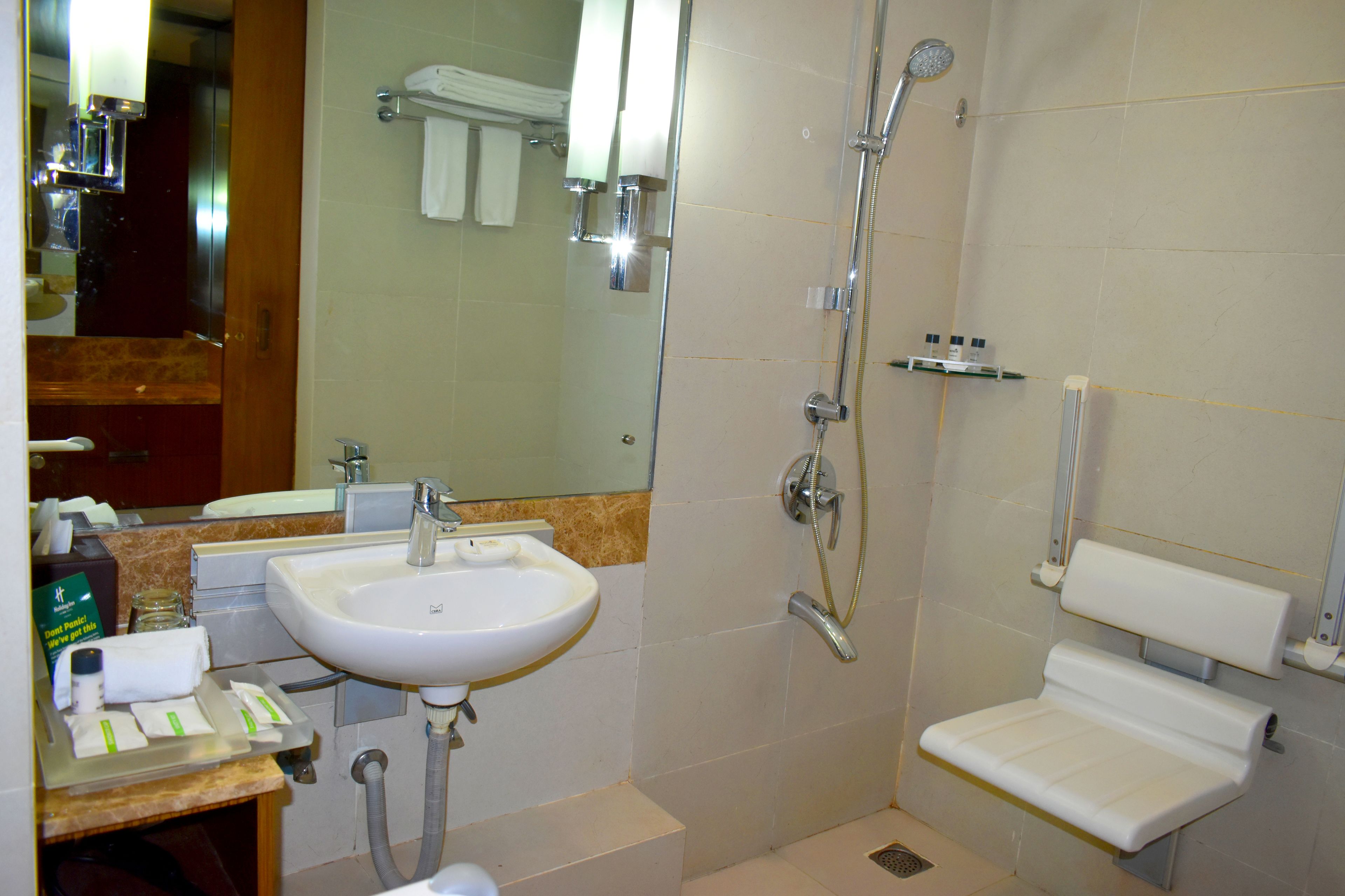 A bathroom with a sink, mirror, shower, and a small bench.