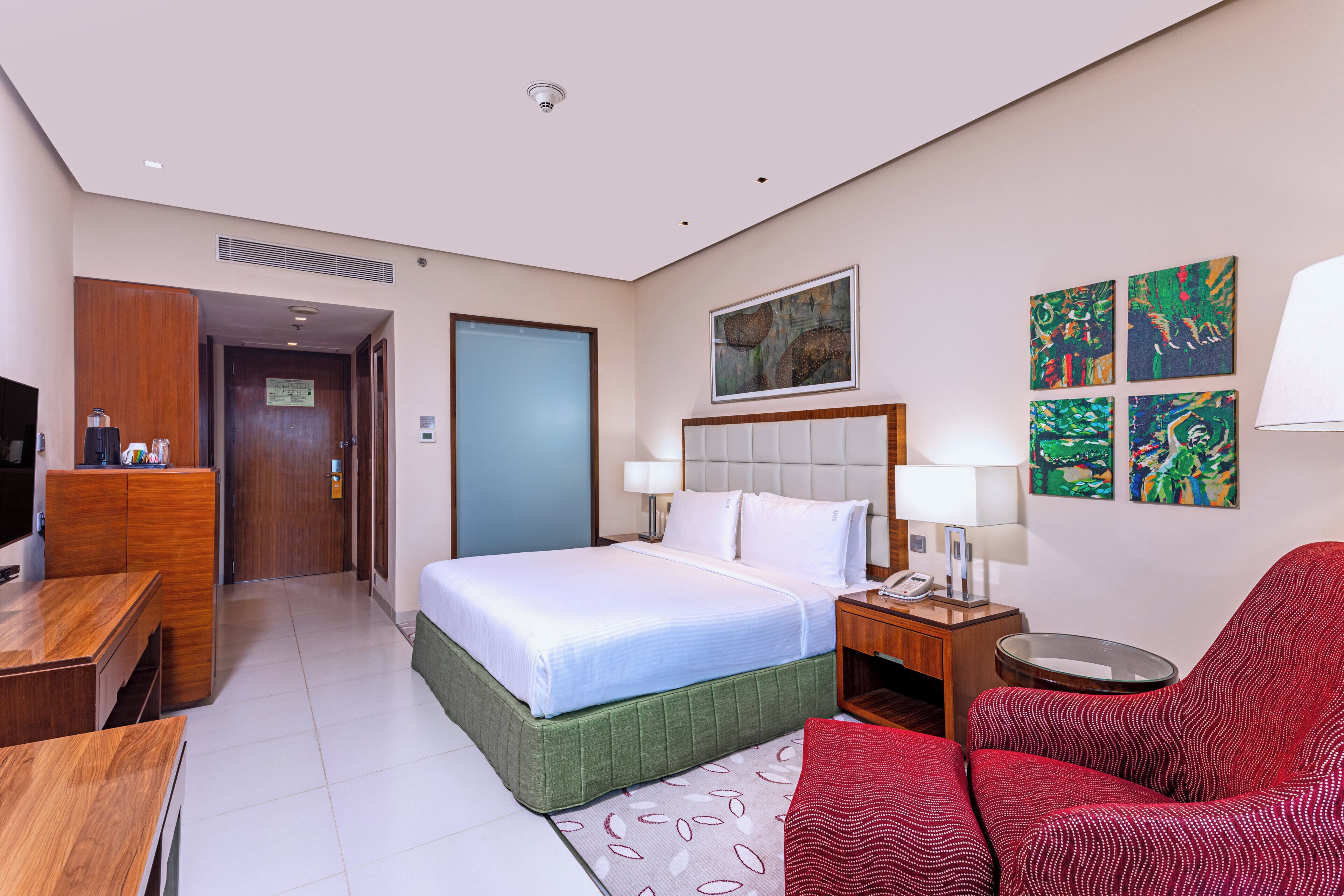 A hotel room with a bed, a desk, a chair, a TV, and artwork on the wall.