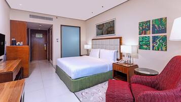 A hotel room with a bed, a desk, a chair, a TV, and artwork on the wall.