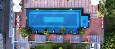 Vista aérea de un hotel con una piscina rectangular grande, zona de estar al aire libre y aparcamiento.