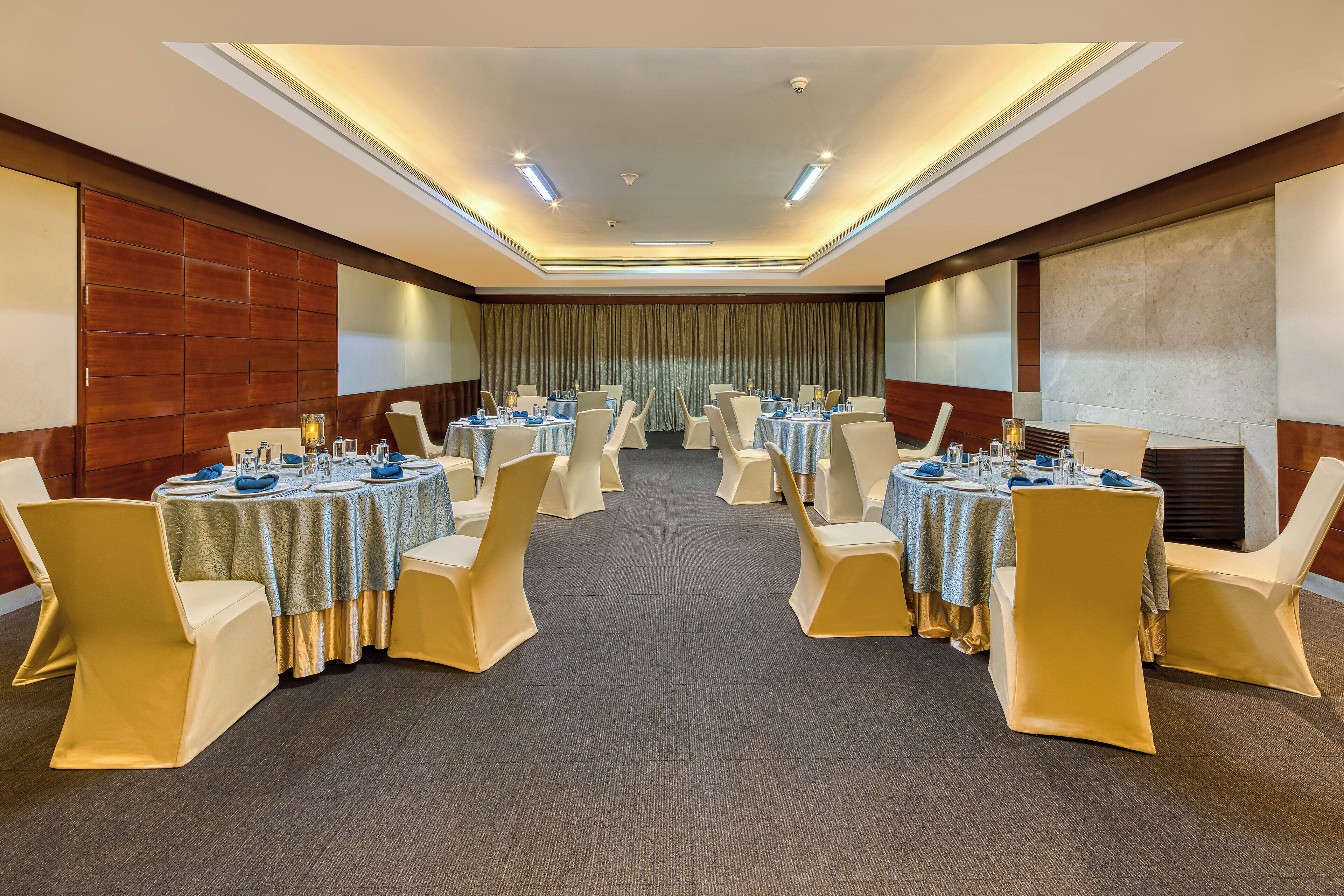 Un salón de conferencias con mesas redondas, sillas color beige y suelo alfombrado.