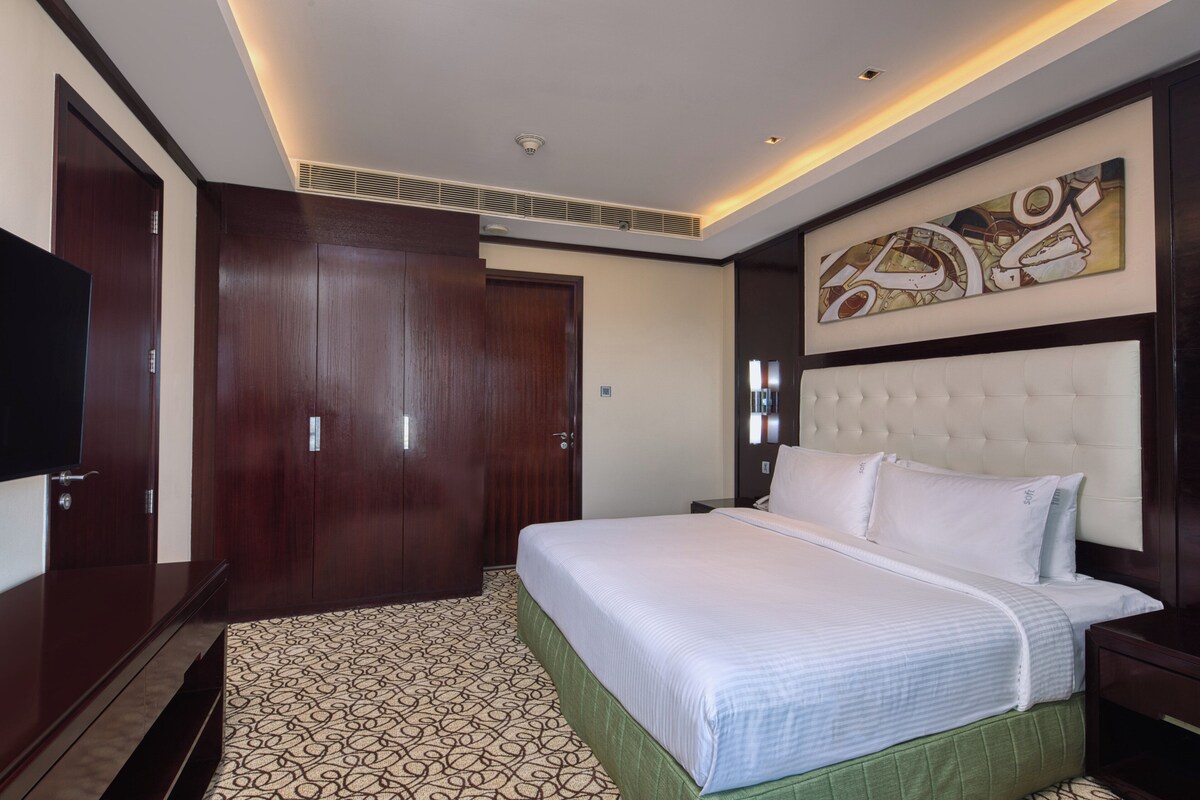 A hotel room with a large bed, a wardrobe, a television, and a wall-mounted artwork.
