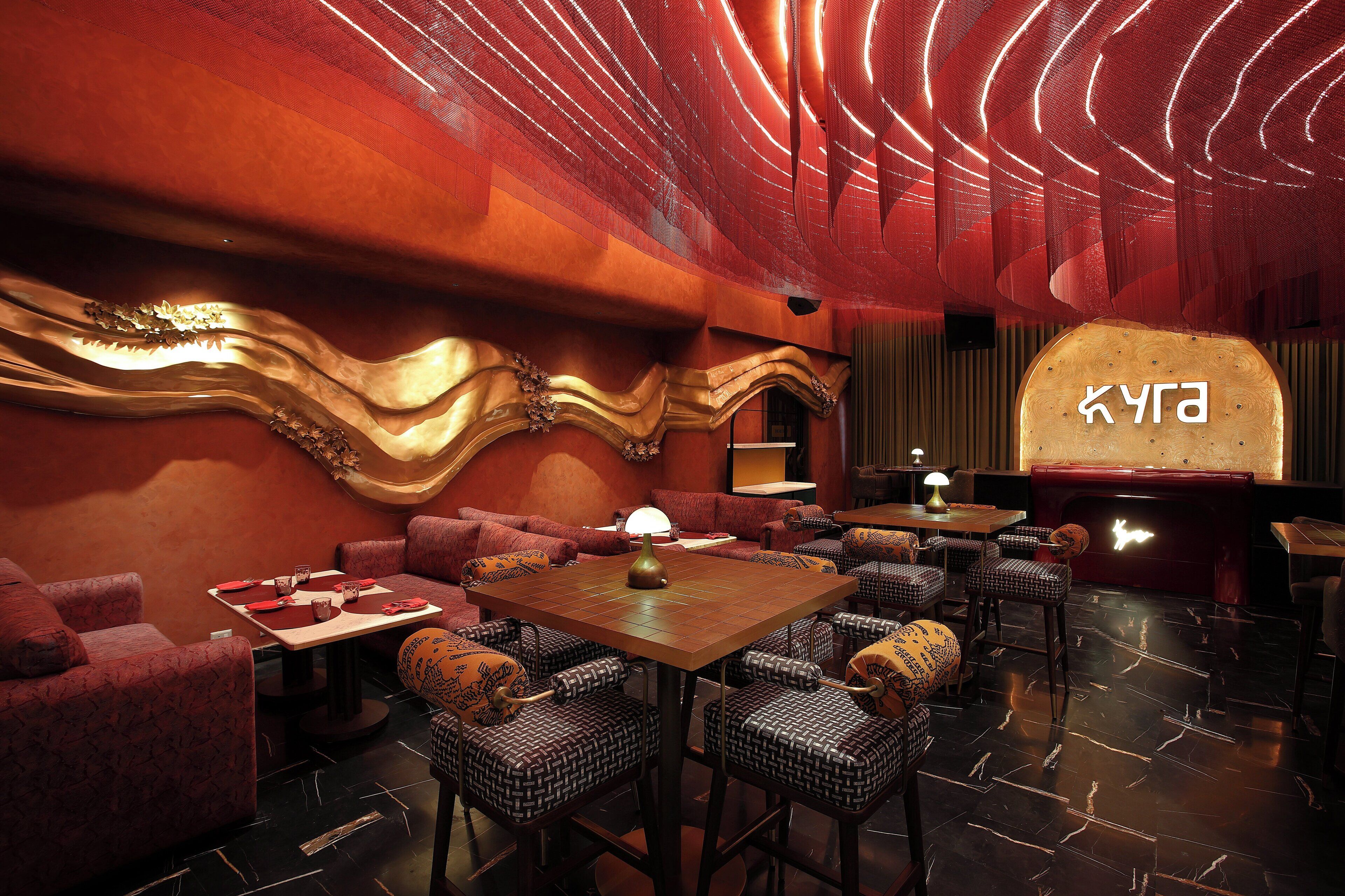 A restaurant with red and gold decor, a wooden table, and patterned chairs.