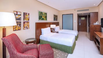 A hotel room with two beds, a red armchair, a small round table, and artwork on the walls.