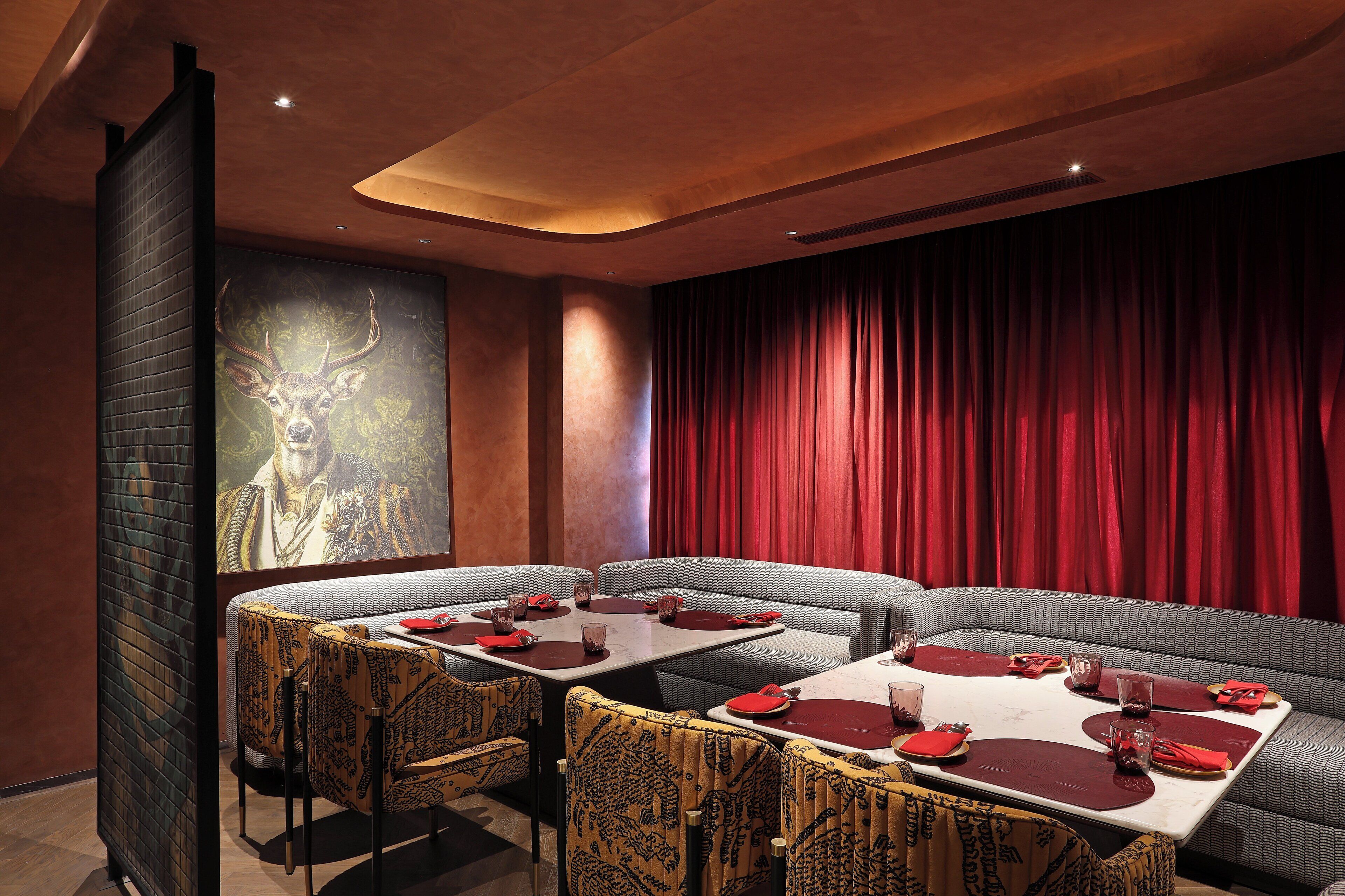 Ein Restaurant mit modernem Interieur, das durch einen roten Vorhang als Hintergrund, gemusterte Stühle und Tische mit roten Servietten und Besteck gekennzeichnet ist.