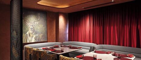 Ein Restaurant mit modernem Interieur, das durch einen roten Vorhang als Hintergrund, gemusterte Stühle und Tische mit roten Servietten und Besteck gekennzeichnet ist.