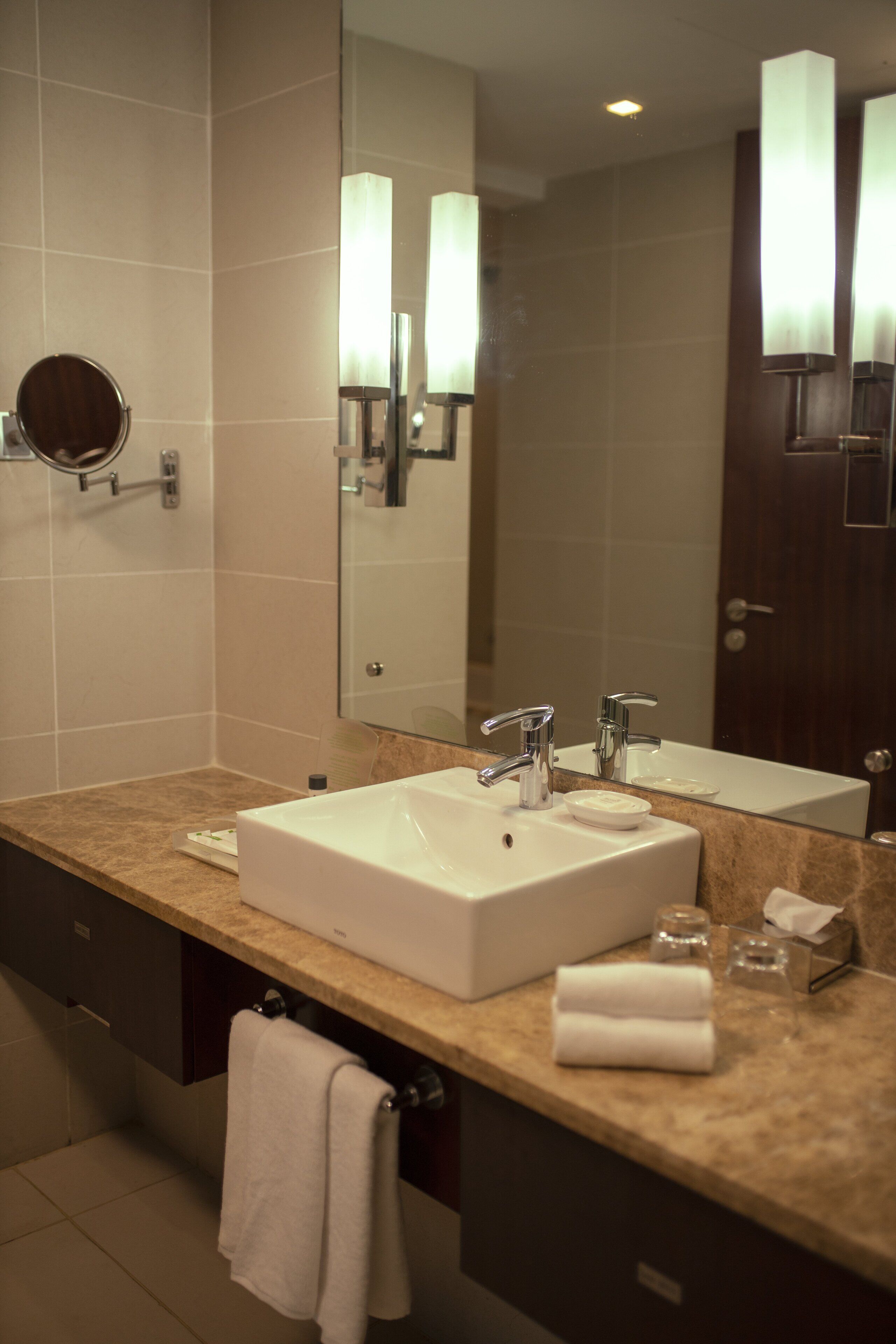 A modern bathroom with a large sink, two faucets, a mirror, and a towel rack.