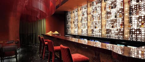 A bar area with a high bar counter, multiple shelves of bottles, and red bar stools.