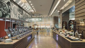 A buffet setup with multiple serving stations, a central serving area, and a variety of food items displayed on shelves. - Holiday Inn Cochin by IHG (Kanayannur)