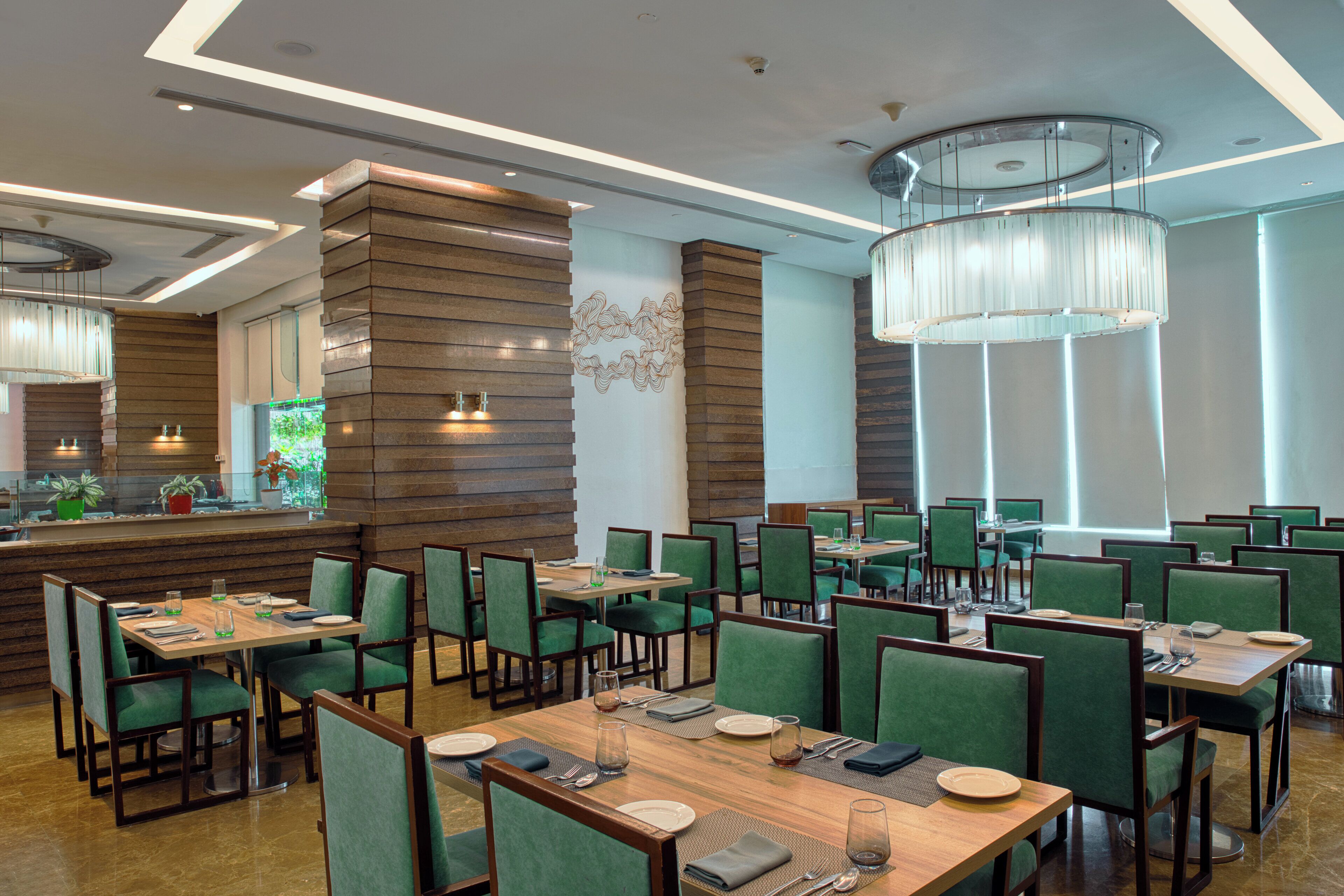 A modern restaurant with wooden tables and green upholstered chairs.