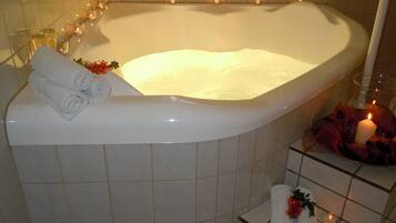 Una bañera grande con múltiples velas, toallas y un arreglo floral.