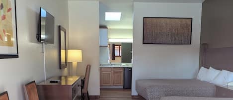 Une chambre d’hôtel équipée d’un bureau, de deux lits, d’une kitchenette et d’une salle de bain visible à travers une porte ouverte.