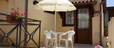A balcony with a table and chairs, a potted plant, and a white umbrella.