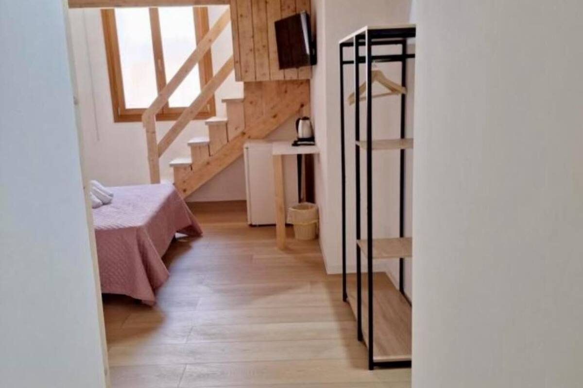 A narrow room with a wooden staircase, a bed, a desk, and a TV mounted on the wall.