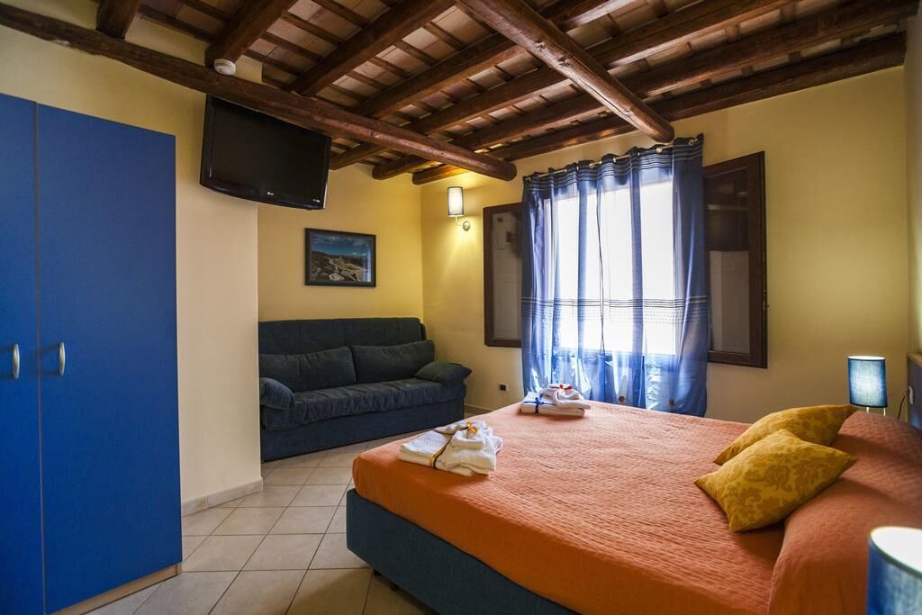 A bedroom with a bed, a blue wardrobe, a sofa, a TV, and a window with curtains.