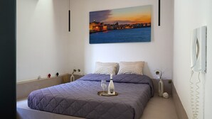 A modern bedroom with a large bed, a cityscape painting, and a bedside table with a vase. - Residence Cortile Mercè (Trapani)