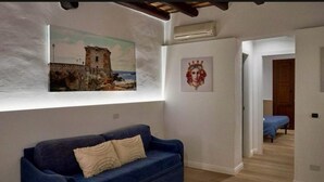 A room with a blue sofa, a painting of a castle, and a crown artwork on the wall. - Residence Cortile Mercè (Trapani)