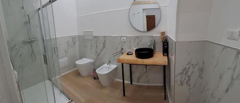 A modern bathroom with a glass shower enclosure, a sink with a mirror, and a bidet.
