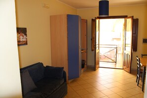 A room with a sofa, a wardrobe, a dining table, and a door leading to an outdoor area. - Residence Cortile Mercè (Trapani)