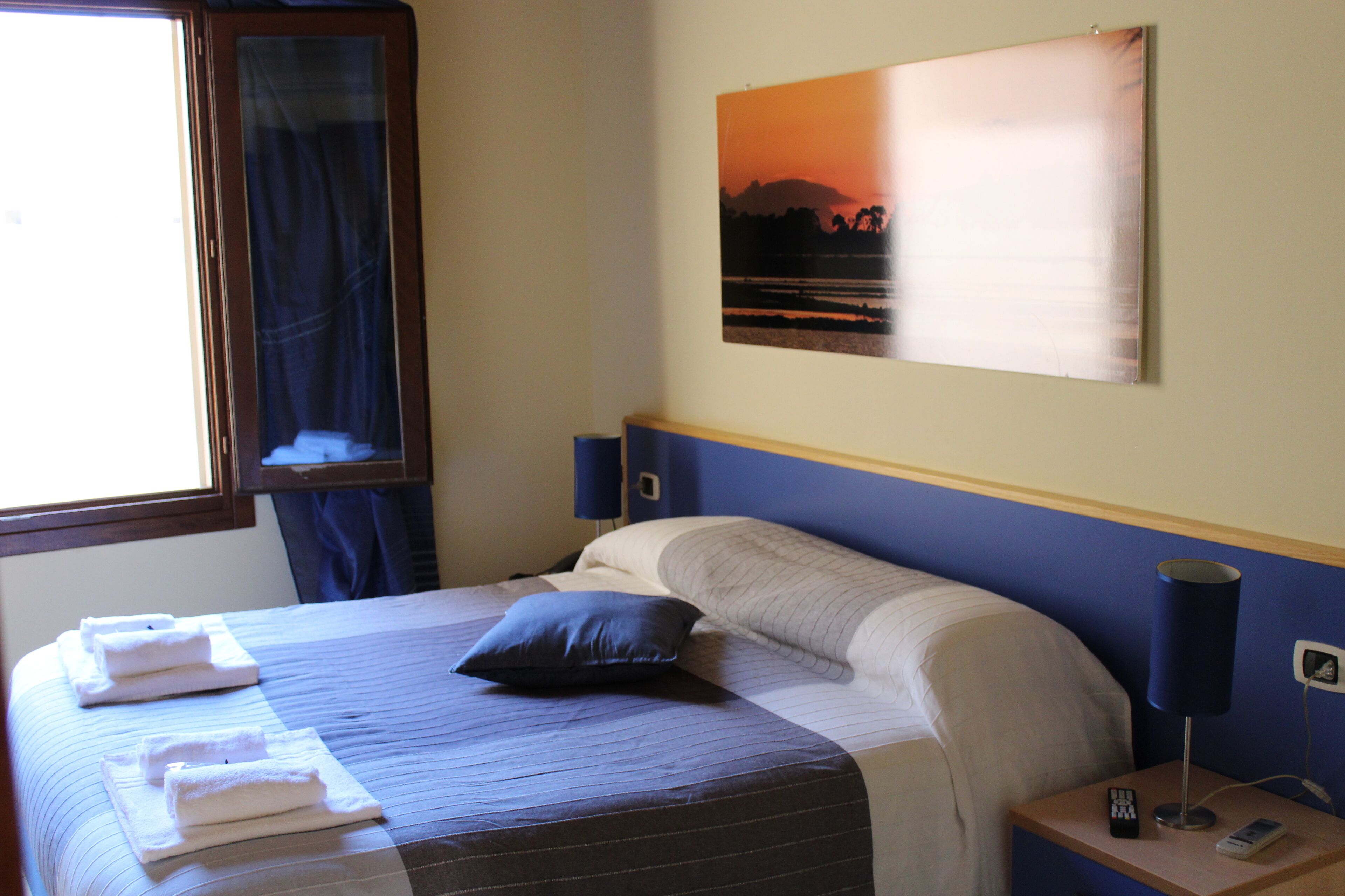 A neatly made bed with towels, a pillow, and a bedside table with a lamp and remote control.