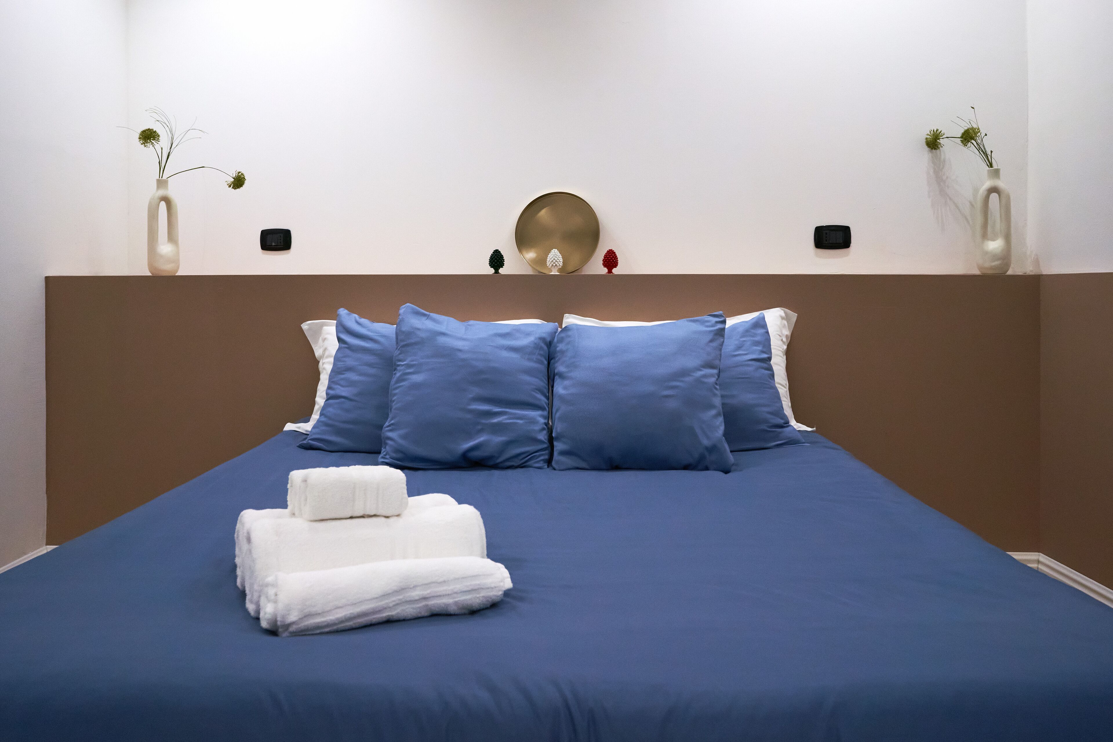 A neatly made bed with blue bedding, white towels, and decorative items on the headboard.