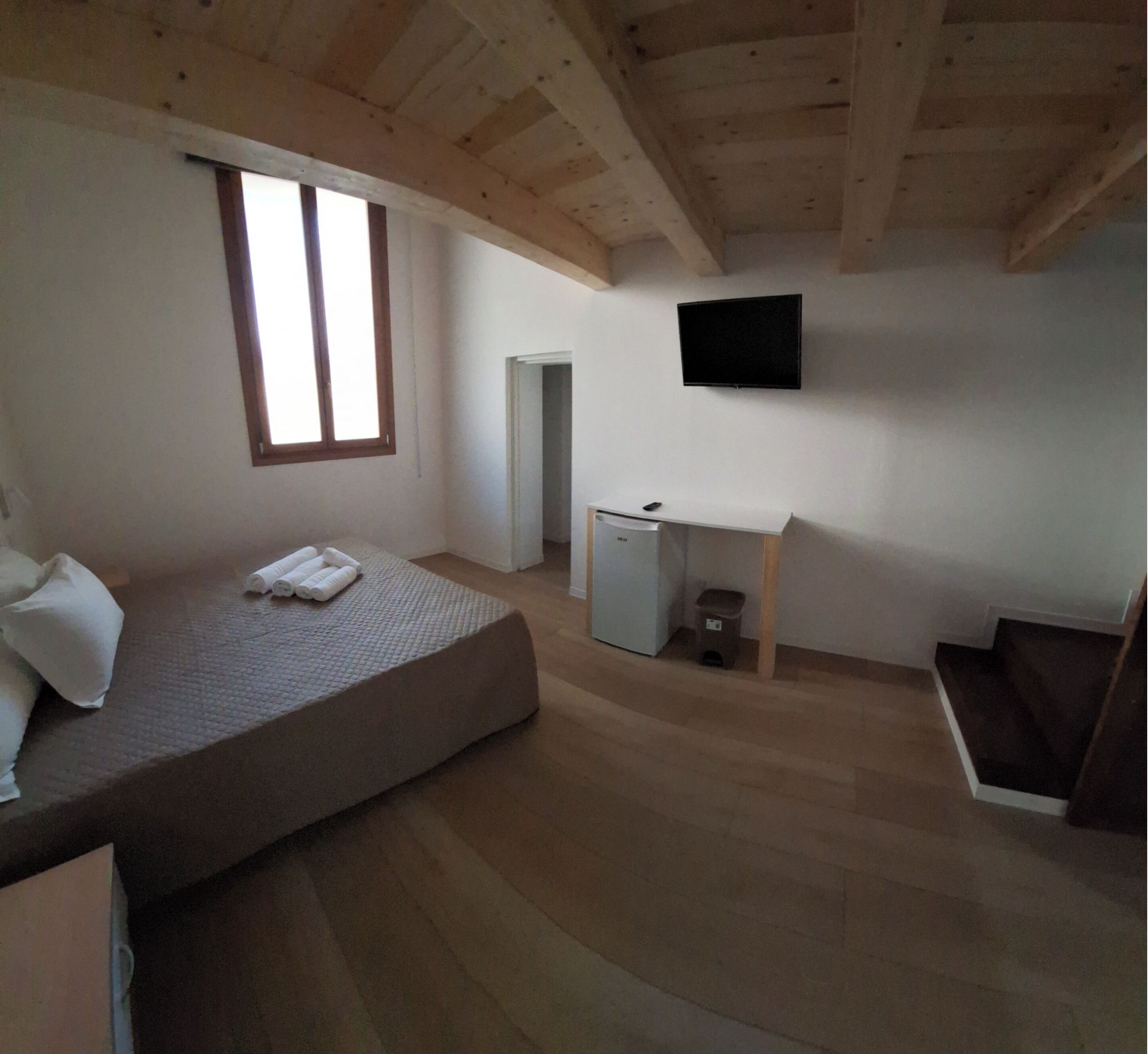 A bedroom with a bed, a desk, a TV, and a window.