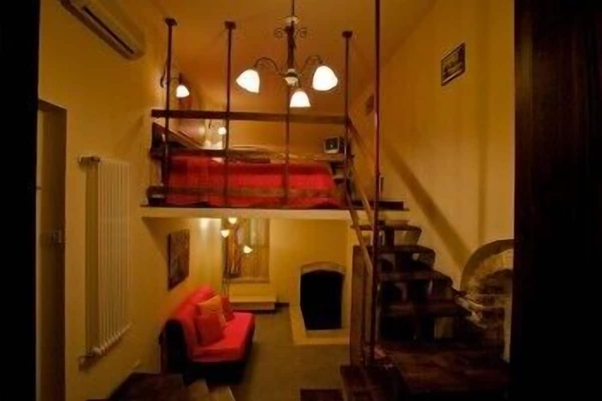 Un pasillo estrecho con un sofá rojo, una escalera y una chimenea.