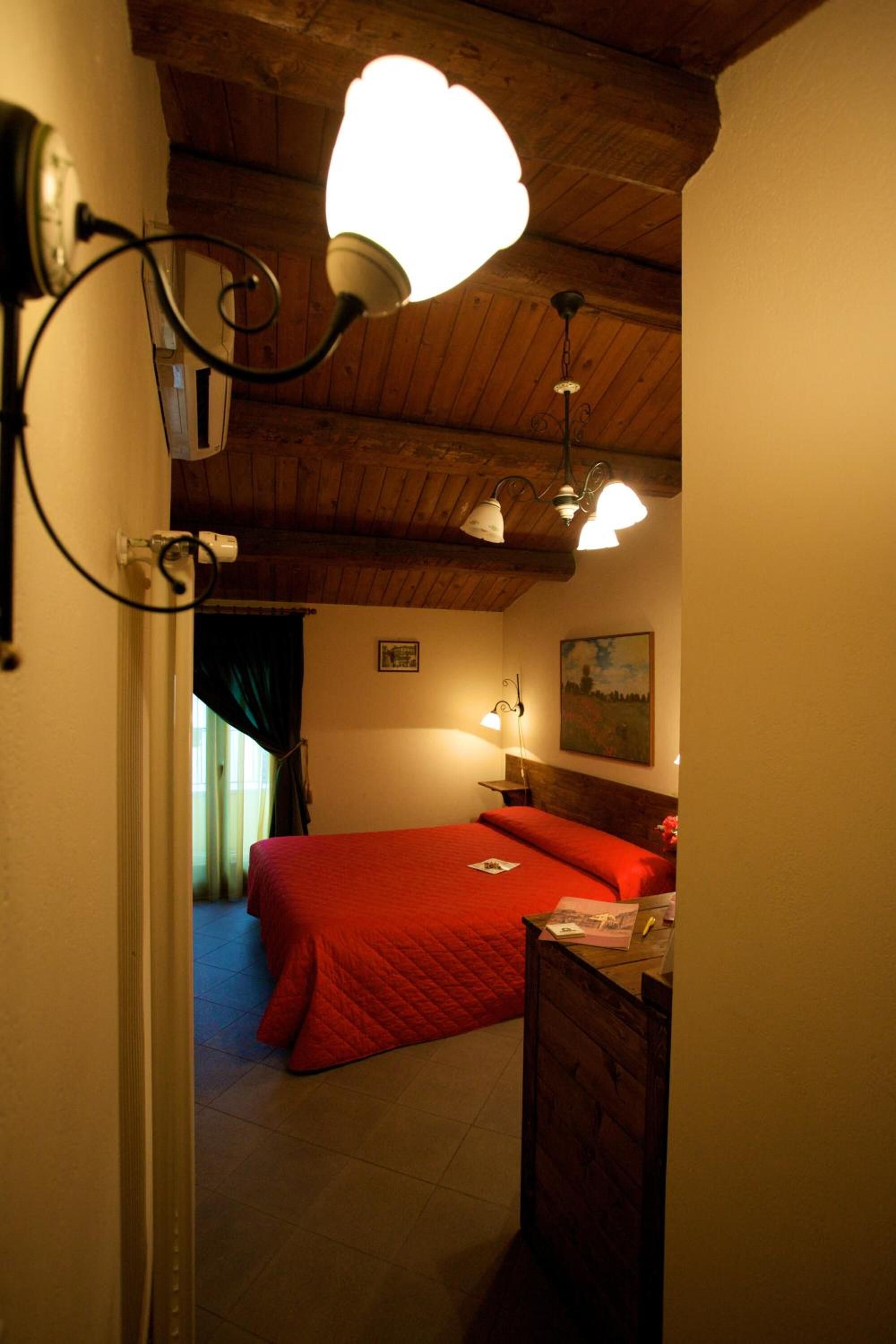 Un dormitorio con techo de madera, una cama roja, una mesita de noche y una lámpara de pared.