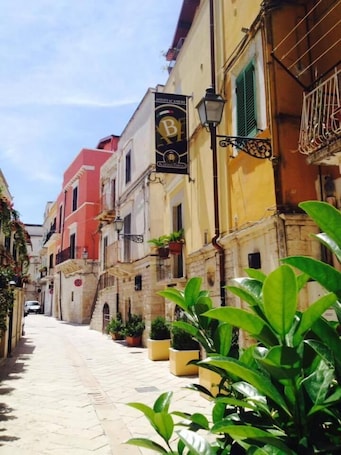 A narrow street lined with colorful buildings, a hanging sign with a logo, and potted plants along the sidewalk.