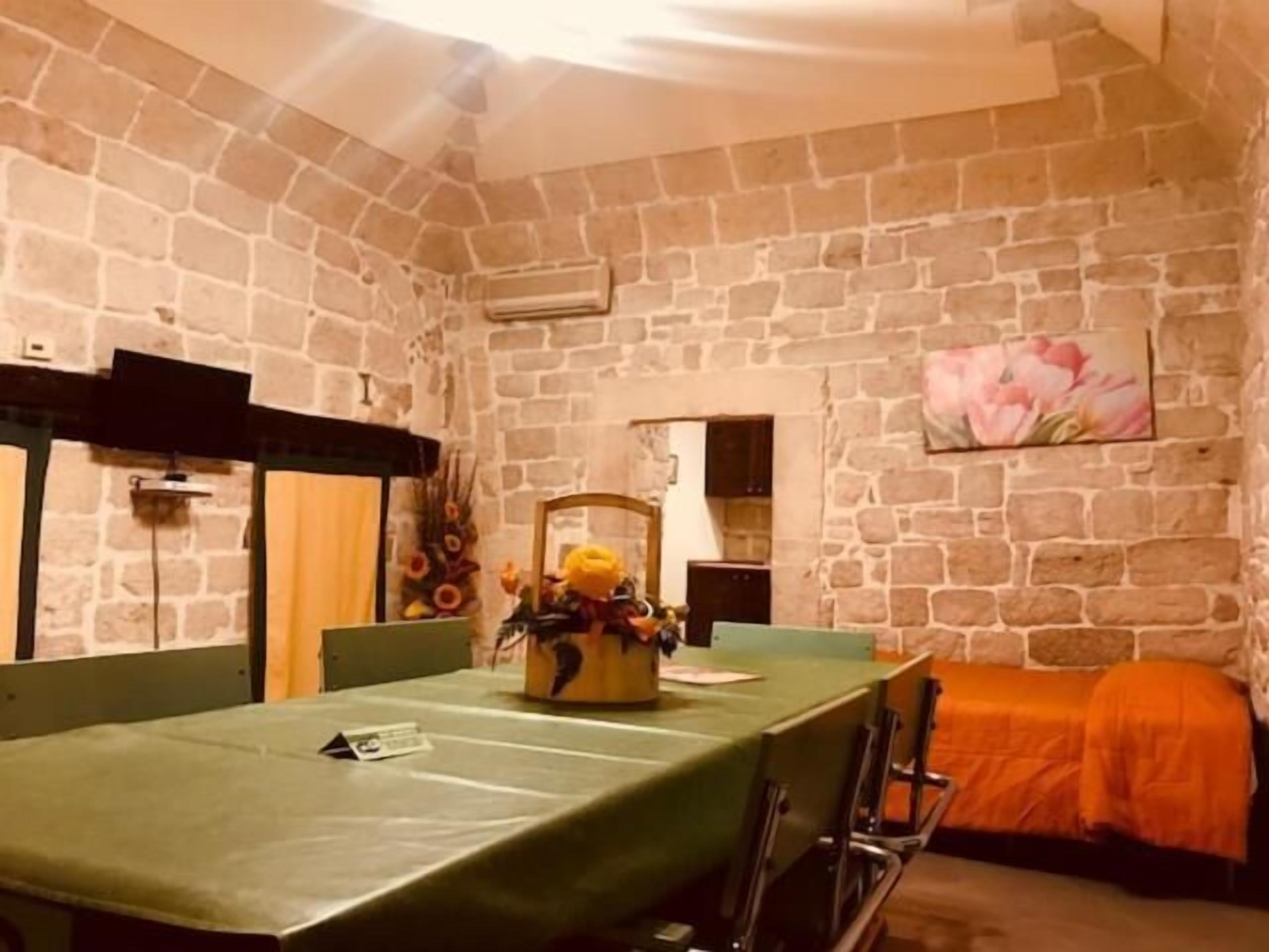 A room with a stone wall, a green table, and a bed with an orange cover.