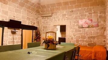 A room with a stone wall, a green table, and a bed with an orange cover.
