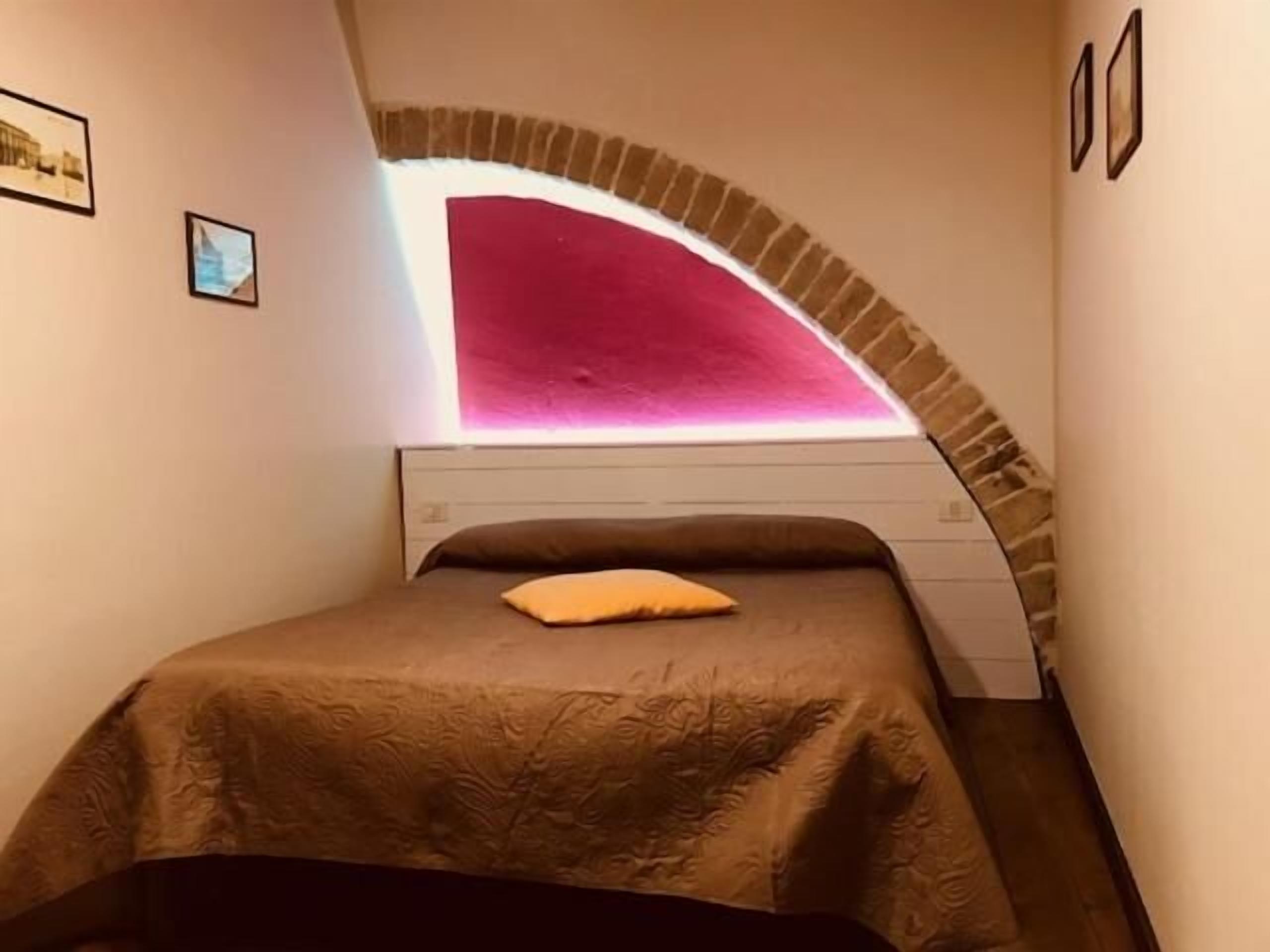 Een slaapkamer met een bed, een kussen en een opvallend roze lichtobject erboven.