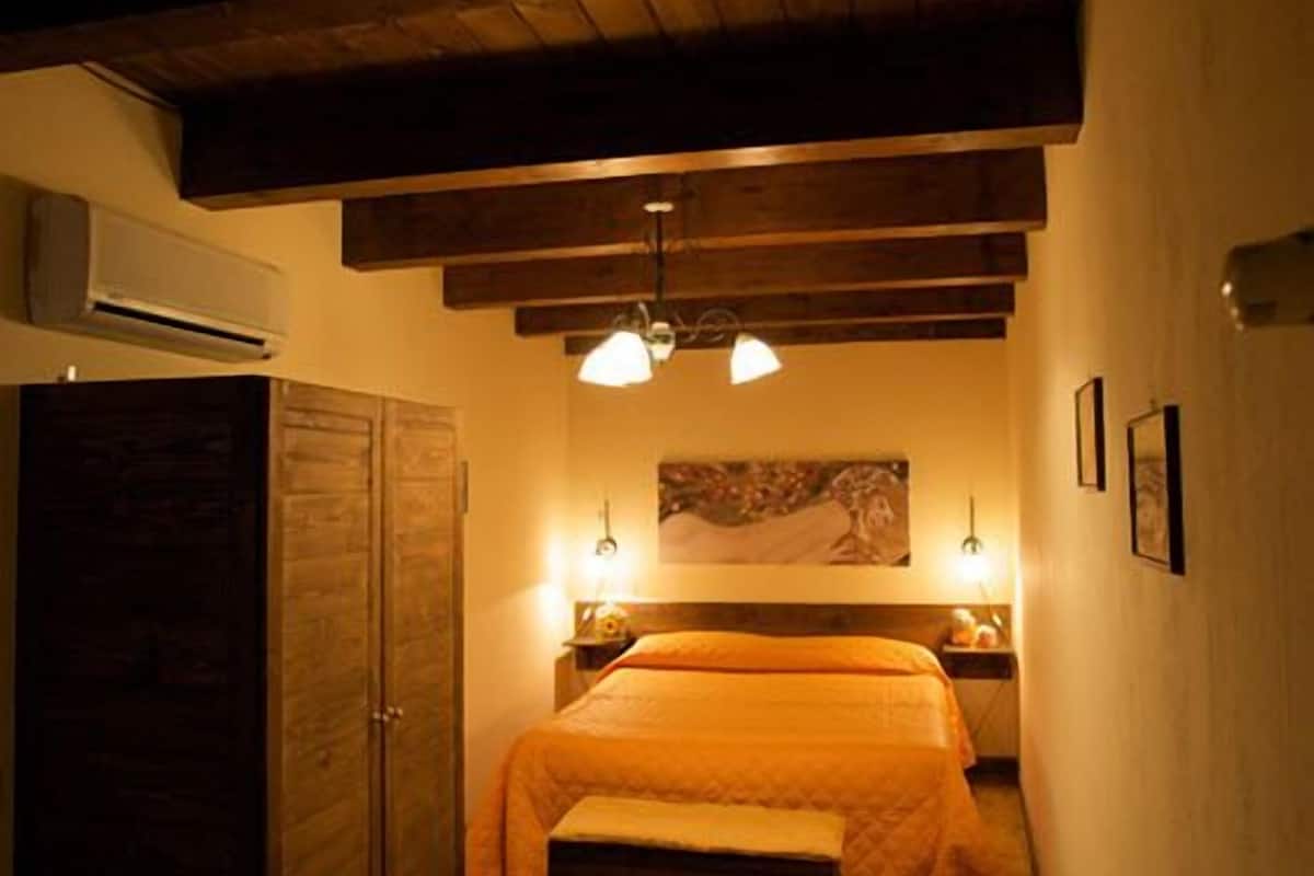 Un dormitorio con techo de madera, una cama con colcha, una mesita de noche y un equipo de aire acondicionado.