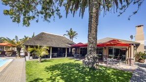A resort with a pool, outdoor seating, and a thatched-roof building. - Excellent Guest House (Cape Town)
