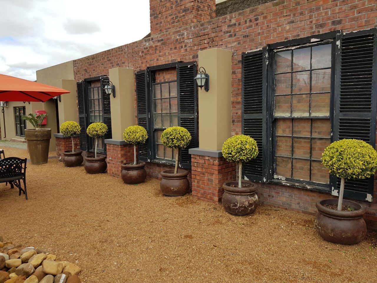 A brick building with multiple windows and planters with topiary trees.
