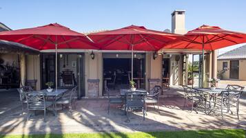 An outdoor patio area with tables and chairs under red umbrellas, a brick wall, and a glass door entrance.