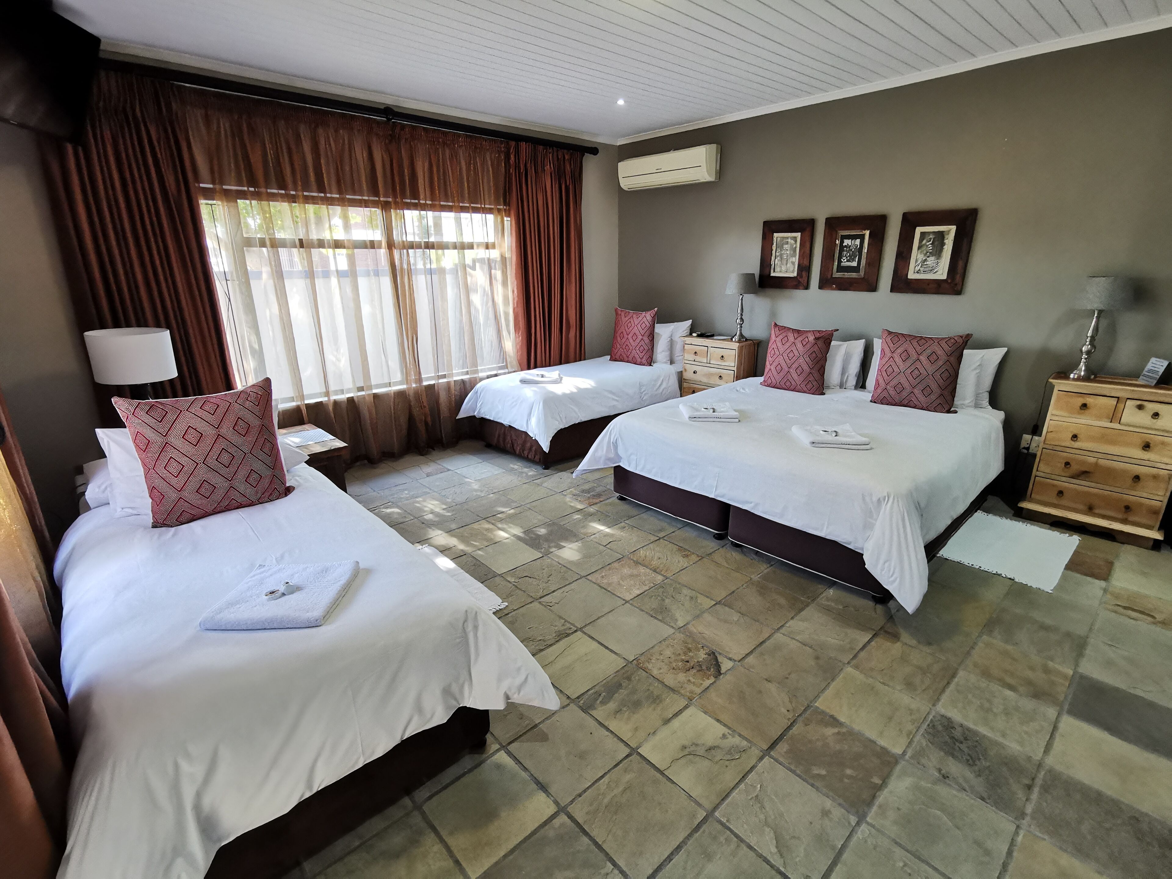 Habitación de hotel con dos camas, una mesita de noche, un aparador y una ventana con cortinas.