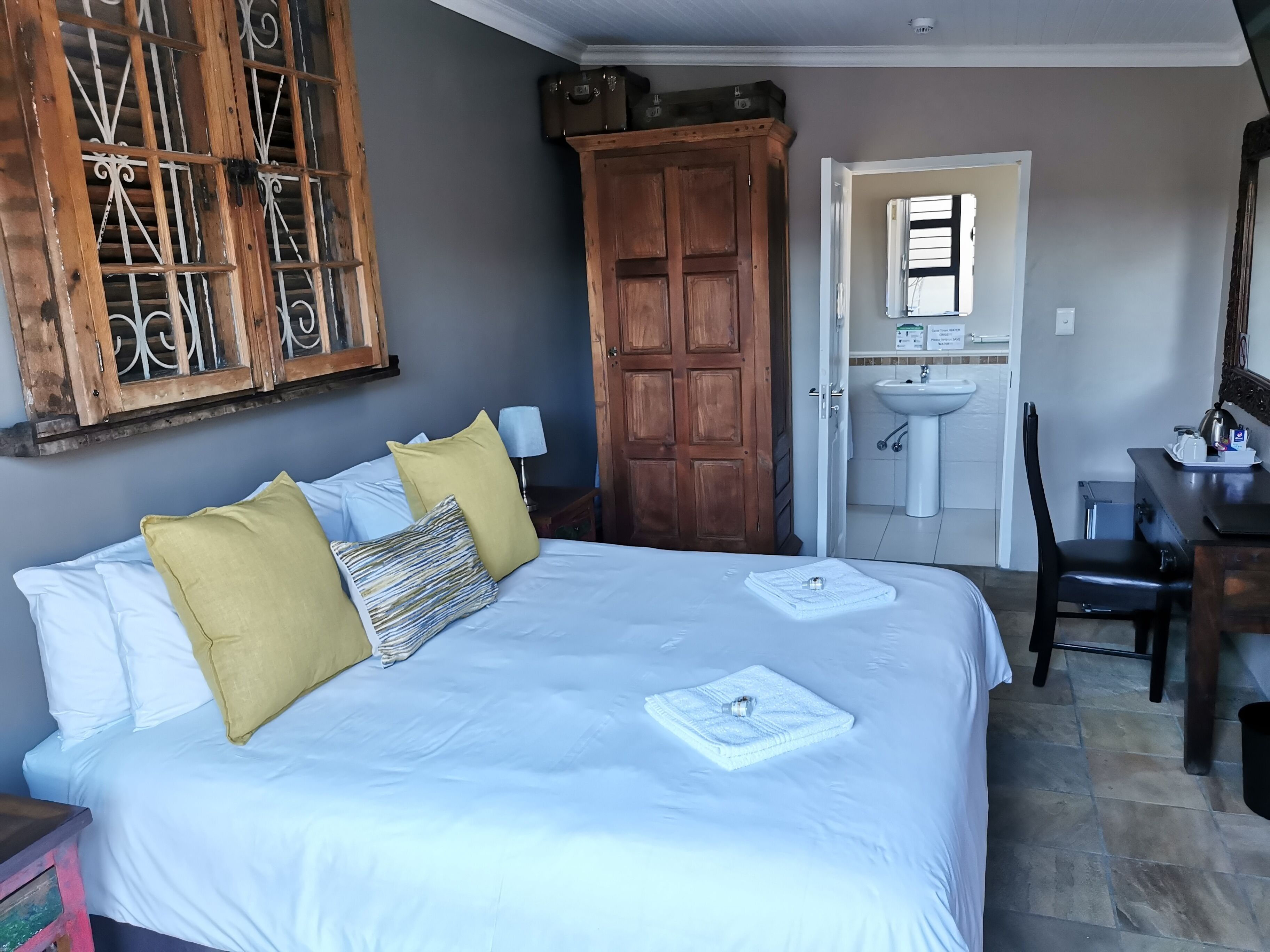 A bedroom with a large bed, wooden wardrobe, and a bathroom visible through an open door.