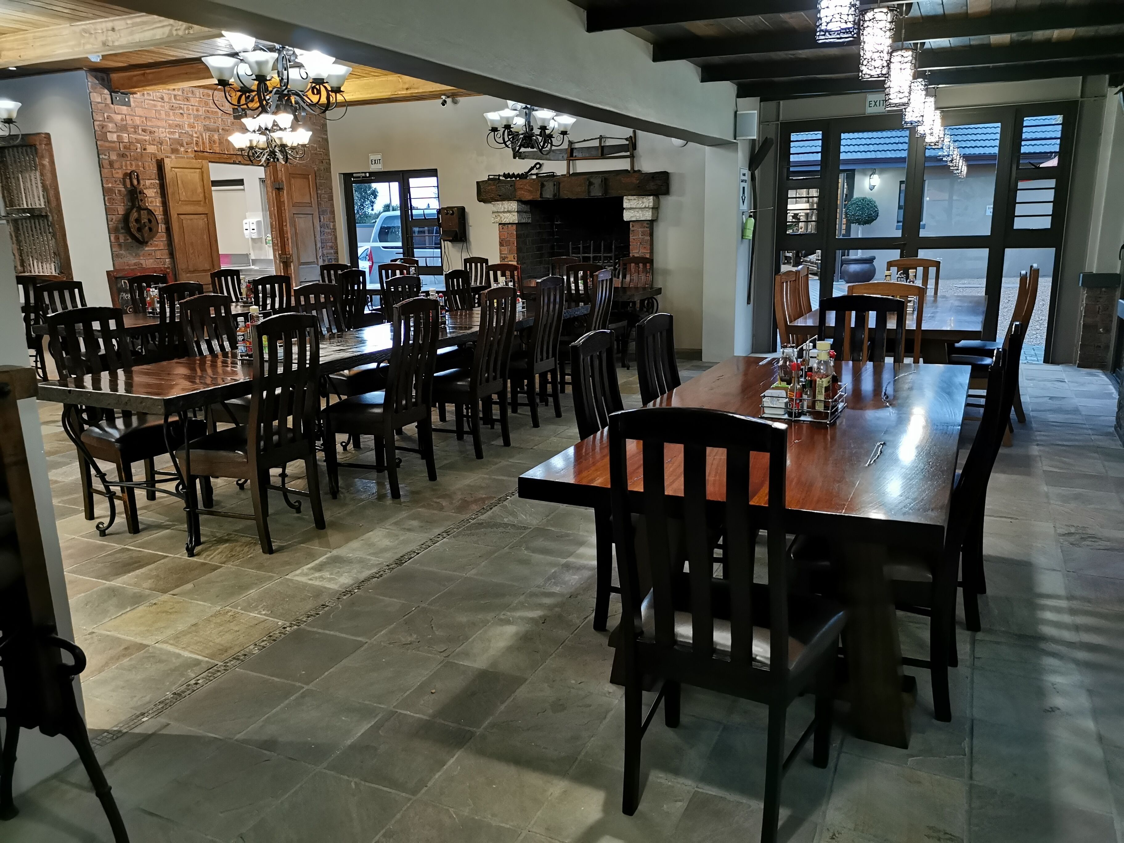 A spacious dining area with multiple wooden tables and chairs, a brick wall, and a fireplace.
