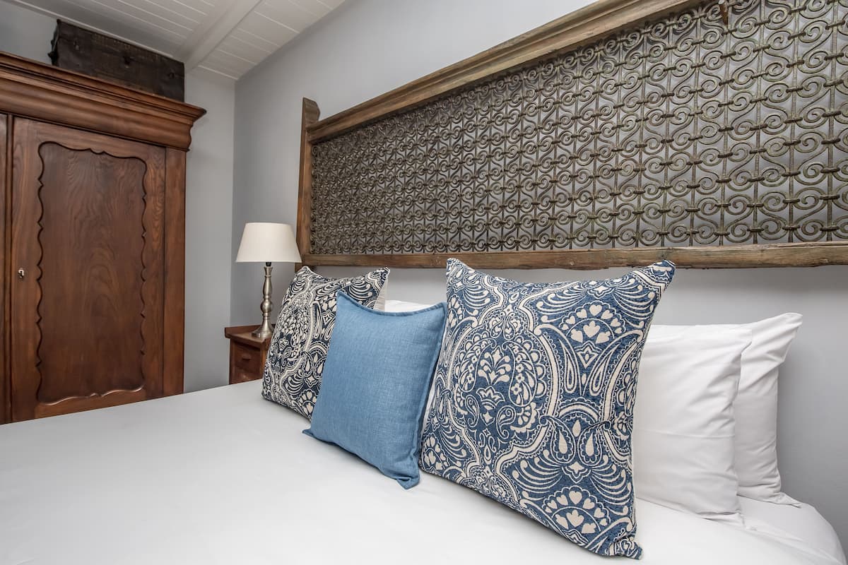Quarto com cabeceira de madeira, almofadas estampadas e mesa de cabeceira com abajur.