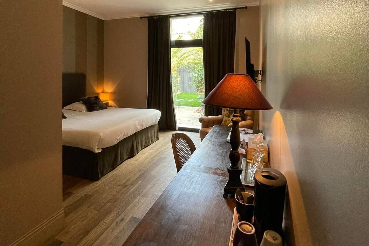 Habitación de hotel con cama, una mesa con lámpara y vistas al exterior.