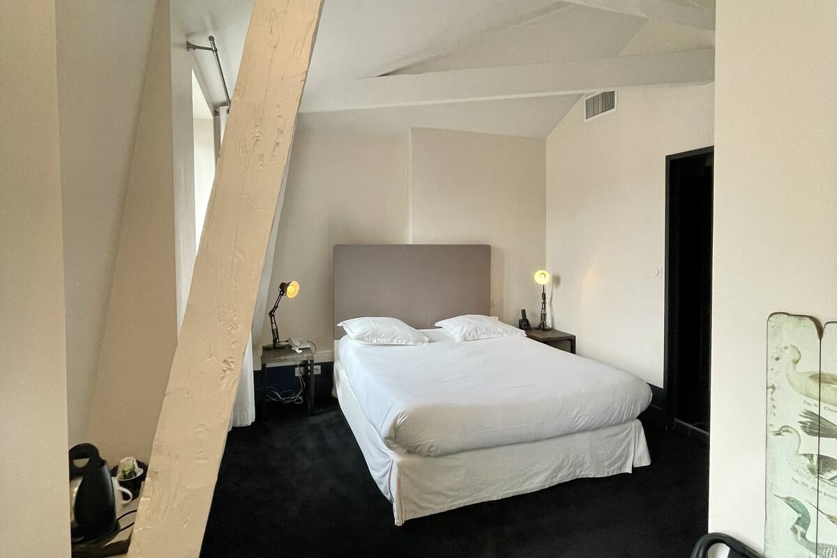 Un dormitorio con una cama grande, una mesita de noche, una lámpara y una ventana.