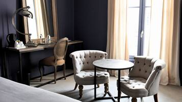 Une chambre d’hôtel comprenant un lit, un bureau avec une chaise, une table ronde avec deux chaises, un grand miroir et une fenêtre avec des rideaux.