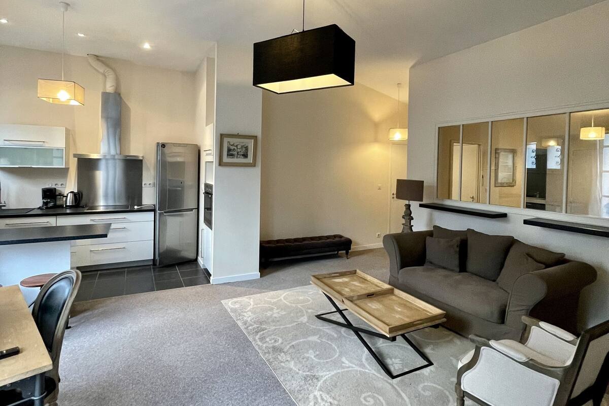 Una sala moderna con un sofá, una mesa de centro y un comedor con sillas. Hay una cocina con un refrigerador y una estufa.