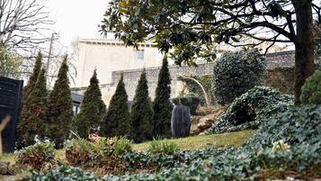 A garden with neatly trimmed hedges, a stone wall, and a building in the background.