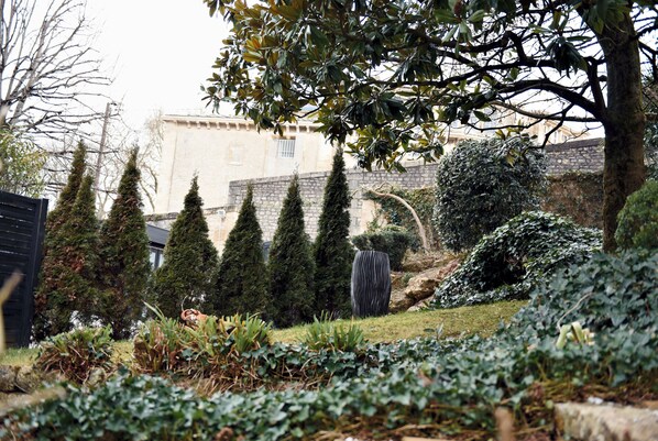 A garden with neatly trimmed hedges, a stone wall, and a building in the background. - Hotel Particulier - La Chamoiserie (Niort)