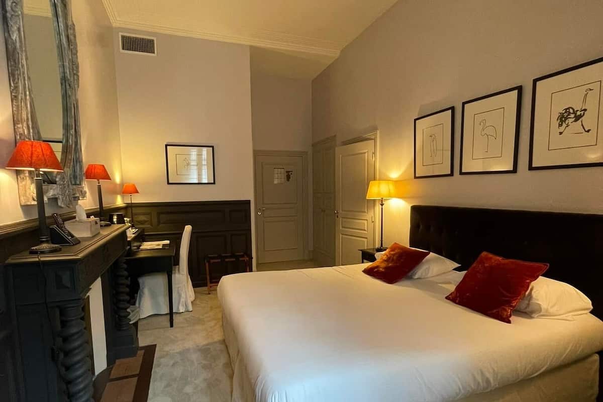 Una habitación de hotel con una cama grande, un escritorio con silla, un espejo y cuadros en la pared.