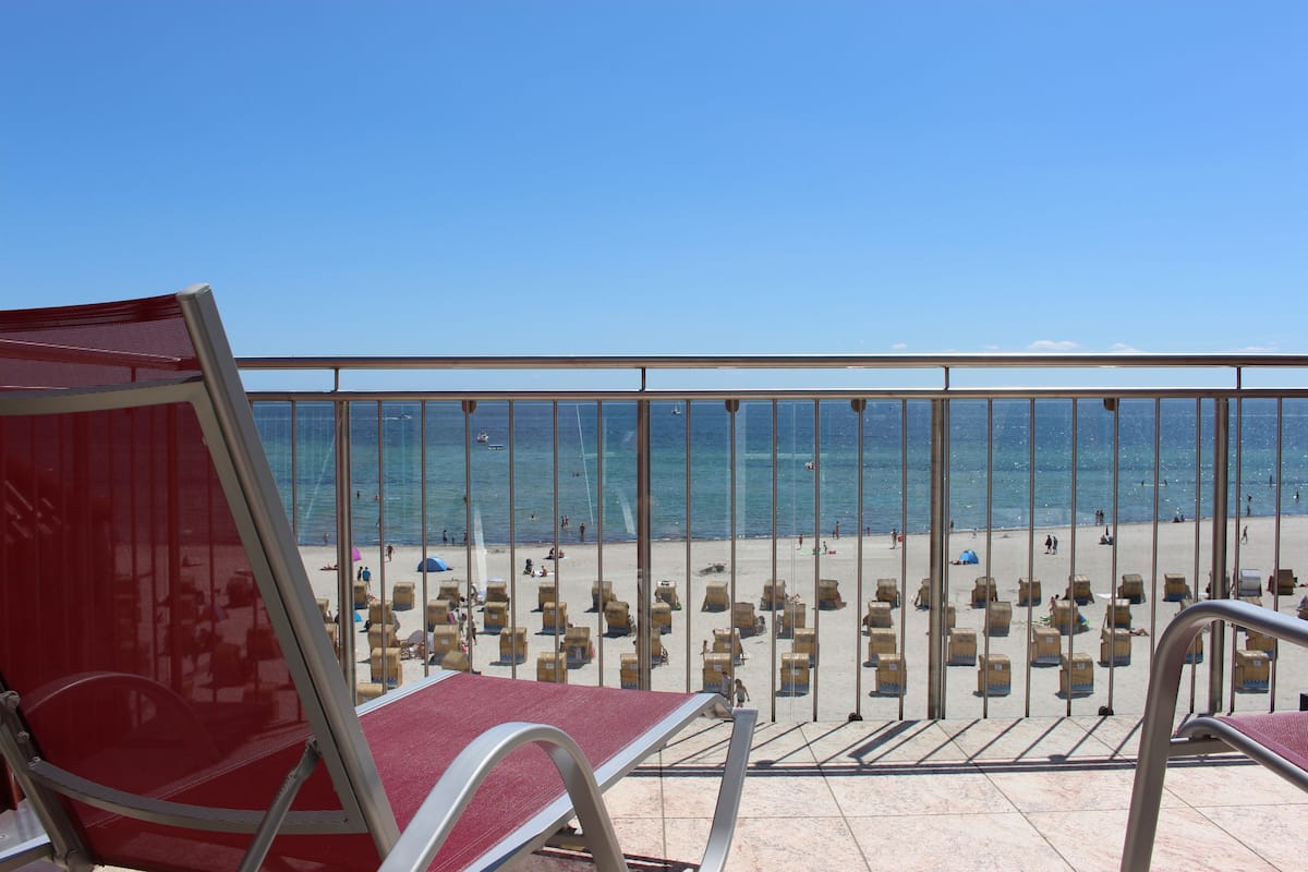 A balcony with red chairs and a view of the beach.