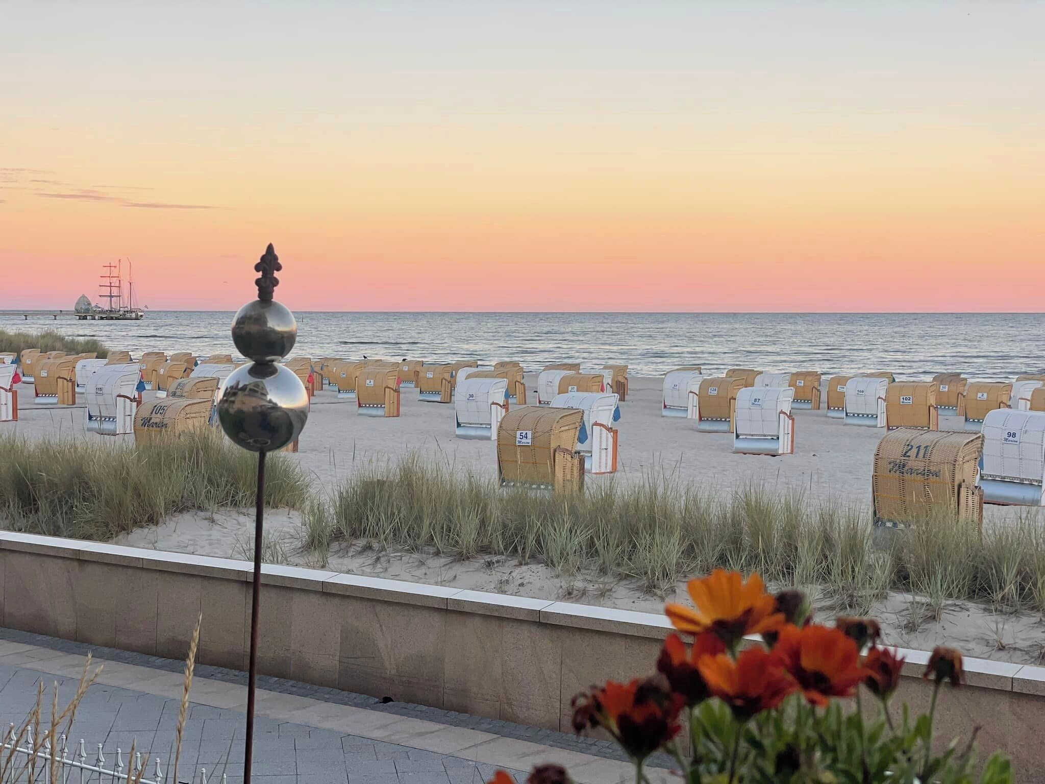 A beach with rows of numbered containers, a metal sculpture, and a distant ship.